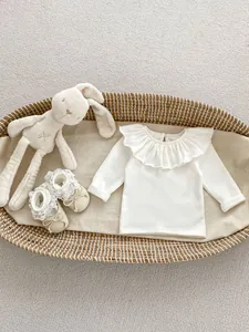Flat lay of white baby long sleeve top with lace collar and toy in a wicker basket