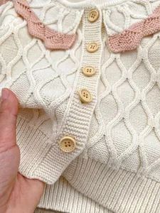 Vue détaillée du gilet en tricot pour bébé crème avec bord rose et boutons en bois