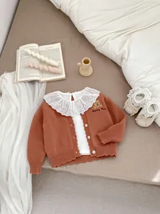 Detail van gebreid babyvest met berenborduursel en witte kanten kraag shirt