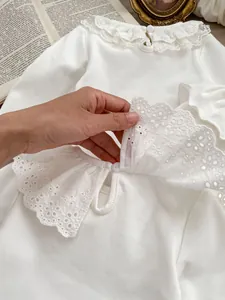 Close-up of white cotton baby top featuring delicate lace collar and button detail