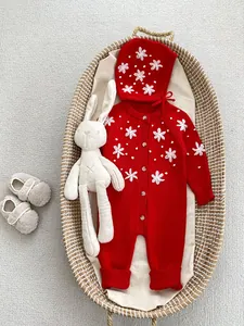 Detail of red knit baby romper with white crochet flowers, matching hat and plush shoes