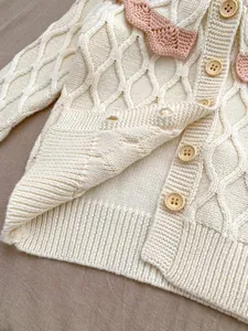 Détail du cardigan bébé en tricot crème avec texture losange et bordure rose
