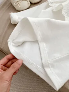 Detail shot of white baby shirt showing fine stitching on lace hem and cotton fabric