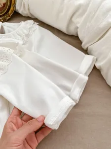 Detailed view of the delicate lace collar and soft cotton fabric on white infant shirt
