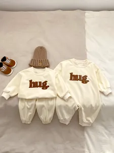 Flat lay of cream baby rompers and sets with brown hug embroidery and knit hat