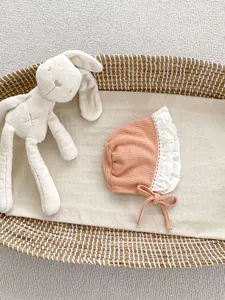 Dettaglio cappello sole neonata con bordo in pizzo bianco e lacci in una culla