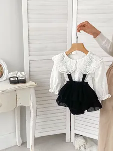 Dettaglio dell'outfit da neonata con colletto ricamato in pizzo e gonna con bretelle