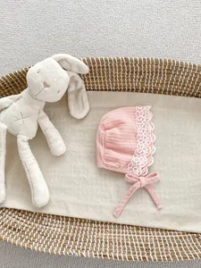 Dettaglio della cuffia neonata in cotone rosa con pizzo floreale bianco e lacci