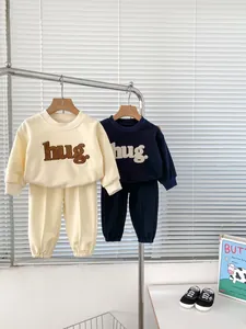 Detail view of cotton baby sweatshirts with 'hug.' embroidery in beige and navy blue