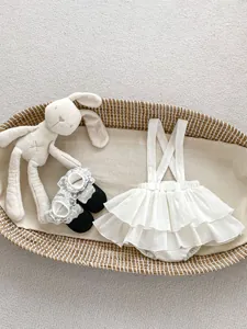 Flat lay of baby white ruffled romper and lace shoes in a woven basket display