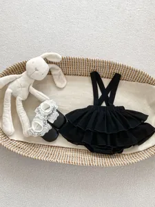 Baby girl black ruffle strap dress with small leather shoes and lace socks on beige carpet