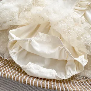 Detailed close-up of cream lace rose pattern and bottom snap buttons on baby romper
