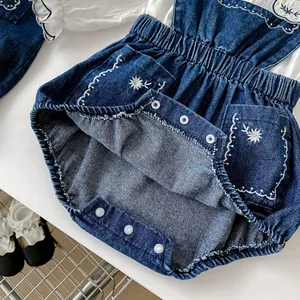 Détail d'une barboteuse bébé en jean brodé avec chemise en dentelle et boutons pression