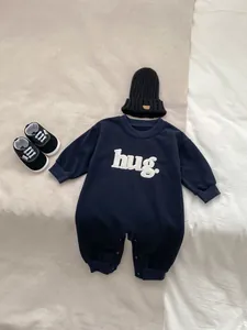 Detailed flat lay of navy baby romper with hug embroidery, knitted hat and infant shoes