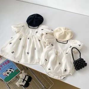 Detail van babyjurk en romper met pofmouwen en zwart geborduurde strikjespatroon