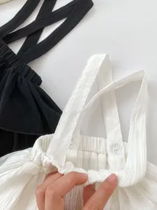 Detail of baby girls' ruffle suspender skirt with elastic waist and button strap texture