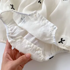 Detail van de drukknoopsluiting en strikborduursels op de babyromper van katoen
