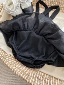 Detail of black cotton linen baby romper dress with ruffle trim in a woven basket