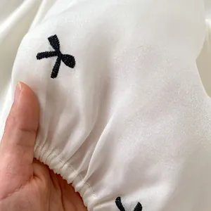 Detail van witte satijnen stof met zwart borduursel en elastische plooien voor babykleding