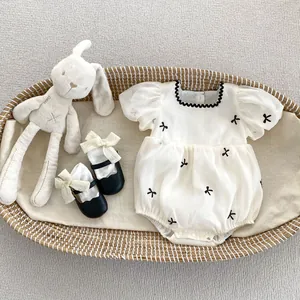 Detail van de babyromper met pofmouwen, strikborduursel en bijpassende schoentjes