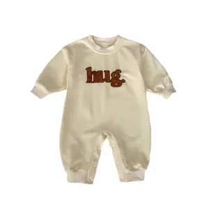 Minimalist cream-colored baby romper with long sleeves and 'hug.' embroidery detail