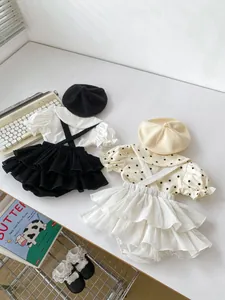 Flat lay of two baby girl summer sets with ruffle overalls and berets on white desk