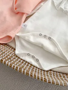 Close-up of baby bodysuit with delicate lace collar and size label in a woven basket