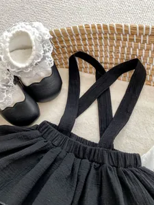 Flat lay of baby girl black ruffled suspender skirt with lace socks and princess shoes