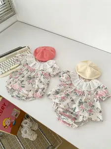 Flat lay of floral baby rompers with lace collars and knit hats on a white table