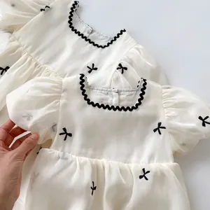 Elegante babyjurk van witte organza met zwart borduursel van strikjes en pofmouwen