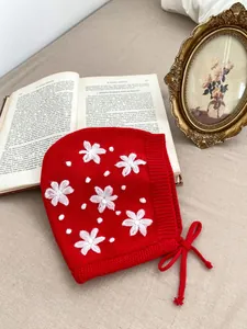 Red knit baby bonnet with white floral embroidery and ties for infants