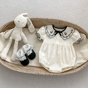 Detail of off-white baby romper with floral embroidered collar and lace shoes in a basket