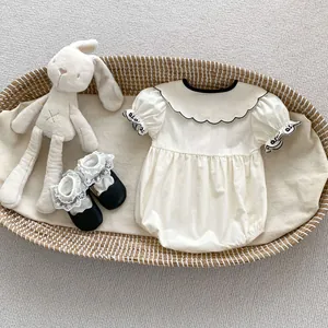 Close-up of beige baby romper with black scalloped collar and cute matching shoes