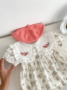 Close-up of floral baby bodysuit with embroidered collar and pink knit beret hat