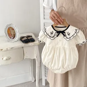 Detail of baby romper with floral embroidered collar and black bow accent on beige cotton