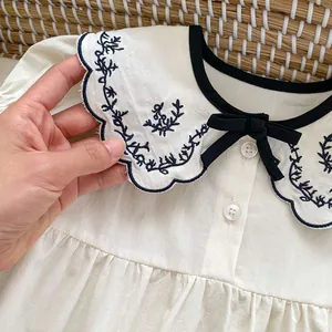 Detail of baby romper featuring blue floral embroidery and a black bow on the collar