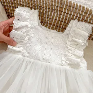 Detalle de vestido de bebé en encaje blanco con bordados florales y falda de tul