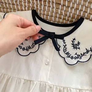 Infant girl beige romper with black doll collar, bow tie and blue floral embroidery