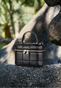 Close-up of black quilted leather box bag with gold zipper and ball pendant