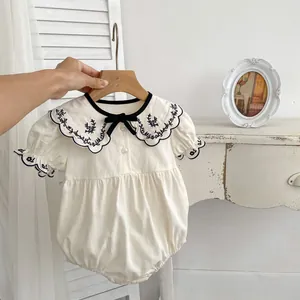 Off-white baby romper with embroidered Peter Pan collar and bow accent on wooden hanger