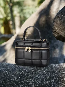 Elegant black quilted leather chain box bag with gold hardware on a natural rock surface