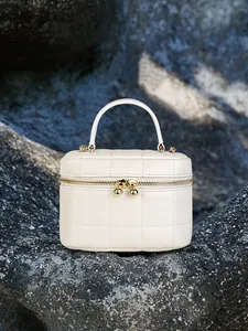 Beige quilted leather mini box bag with gold metal hardware and top handle on stone