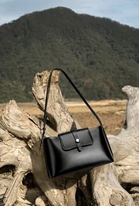 Detailansicht der schwarzen Leder-Achseltasche mit Metallschnalle vor Naturkulisse