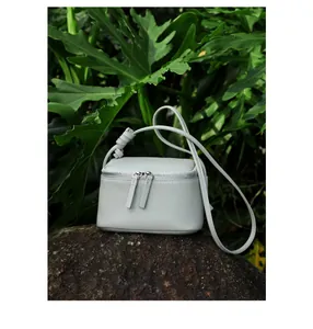 Détail du sac bandoulière en cuir grainé gris avec double zip sur un fond de roche