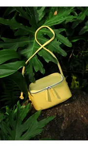 Détail du sac bandoulière en cuir jaune citron posé sur un rocher brun en plein air