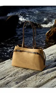 Detailed close-up of brown suede tote bag with leather handle against coastal background
