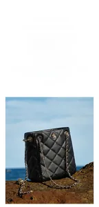 Detail of black quilted bucket bag with golden flower logo and chain strap on sea rocks