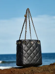 Quilted black leather chain bucket bag with golden camellia buckle on coastal rocks