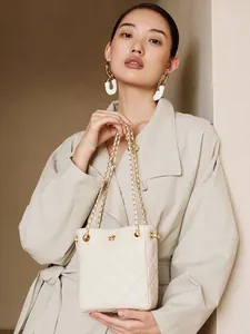 Chic quilted beige crossbody bag with gold chain strap shown on person in a modern interior