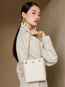 White quilted bucket bag with golden flower logo and chain strap on a stylish model